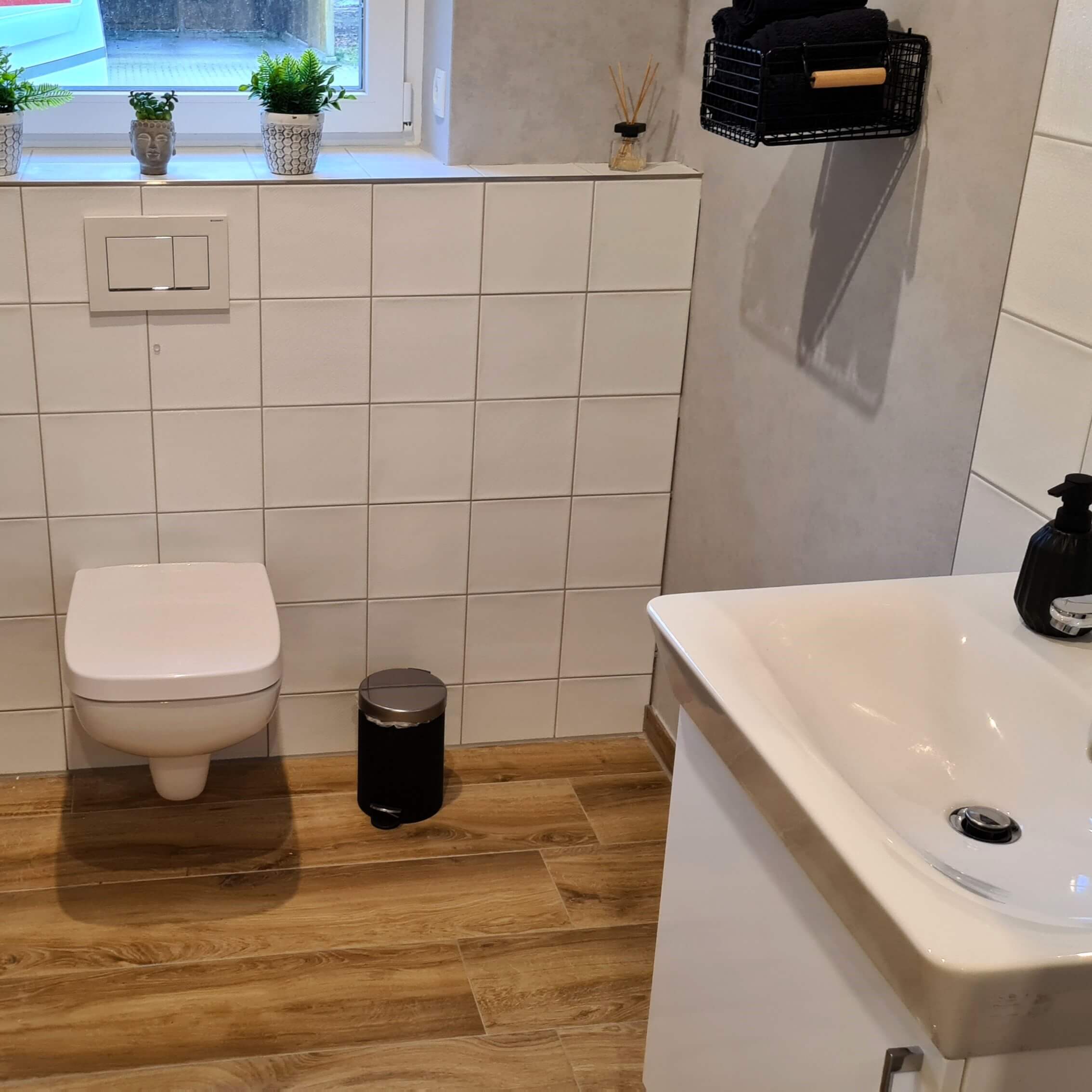 Toilette mit weißen Wandfliesen und braunen Bodenfliesen sowie einem Waschbecken.
