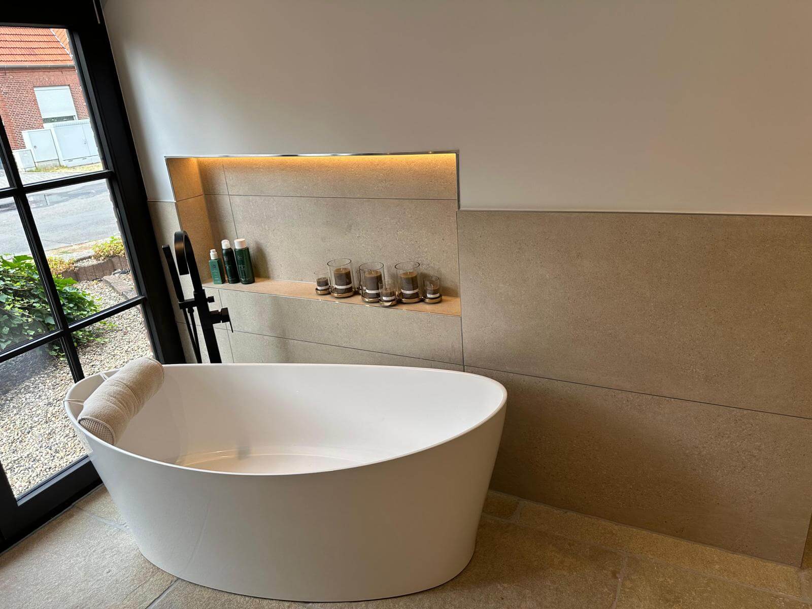 Badewanne neben einer Wand aus Sandstein mit eingebauter und beleuchtetet Ablage, Blick nach draußen