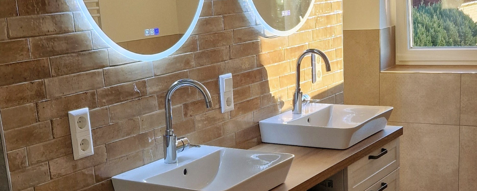 Wand mit rotem Klinker im Badezimmer und runden Spiegeln mit blauem LED Licht (Rand) sowie zwei Waschbecken.